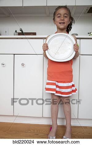 Picture - Caucasian girl holding empty plate in kitchen. Fotosearch