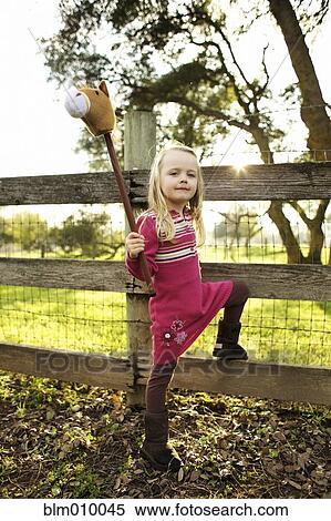 Stock Photography - Caucasian girl holding stick horse near fence. Fotosearch