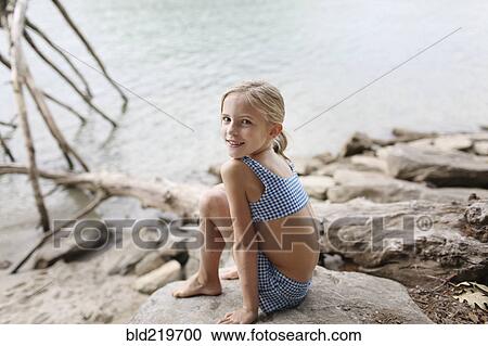 Stock Image - Caucasian girl in bikini sitting by remote lake. Fotosearch