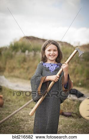Stock Image - Caucasian girl in chain mail carrying hatchet in backyard. Fotosearch