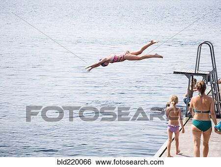 Stock Photograph - Caucasian girl jumping from diving board into lake. Fotosearch