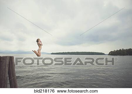 Stock Photograph - Caucasian girl jumping in remote lake. Fotosearch