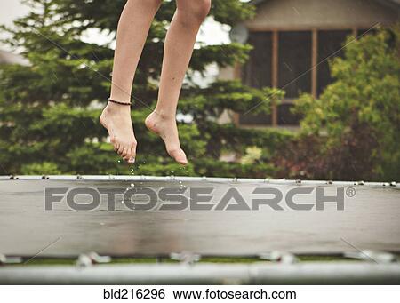 Stock Photograph - Caucasian girl jumping on wet trampoline. Fotosearch