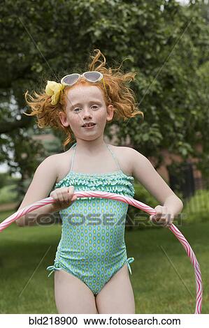 Stock Image - Caucasian girl jumping with plastic hoop in field. Fotosearch