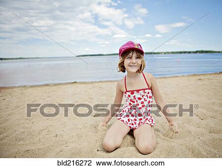Stock Image - Caucasian girl kneeling on beach. Fotosearch