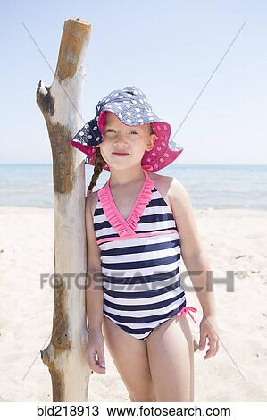 Stock Image - Caucasian girl leaning on wooden pole on beach. Fotosearch