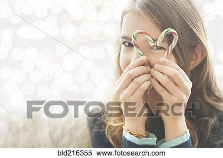 Stock Photography - Caucasian girl looking through heart-shape with candy canes. Fotosearch