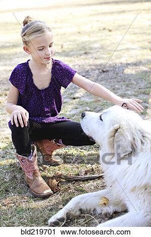 Stock Image - Caucasian girl petting dog in field. Fotosearch