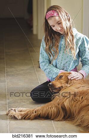 Stock Image - Caucasian girl petting dog on floor. Fotosearch