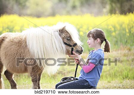 Stock Image - Caucasian girl petting pony in rural field. Fotosearch
