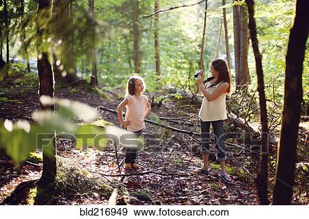 Stock Photo - Caucasian girl photographing sister in forest. Fotosearch