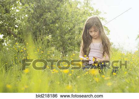 Stock Photograph - Caucasian girl picking flowers in rural field. Fotosearch