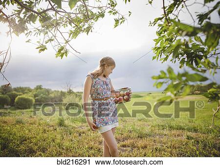 Stock Image - Caucasian girl picking fruit in orchard. Fotosearch