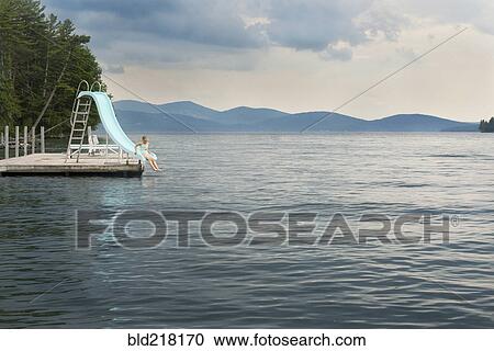 Stock Image - Caucasian girl playing on slide over remote lake. Fotosearch
