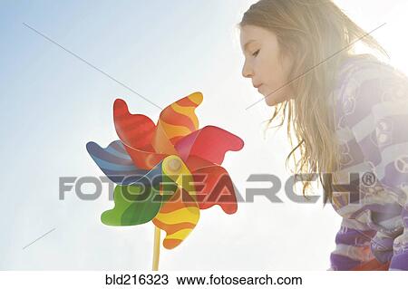 Stock Image - Caucasian girl playing with pinwheel under blue sky. Fotosearch