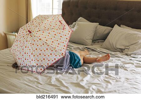 Stock Image - Caucasian girl playing with umbrella on bed. Fotosearch