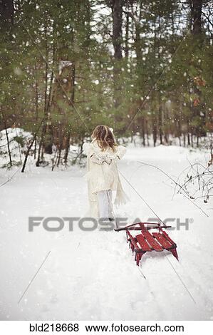 Stock Photo - Caucasian girl pulling sled in snowy field. Fotosearch