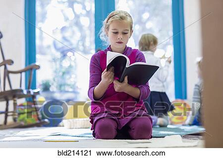 Stock Image - Caucasian girl reading book on floor. Fotosearch