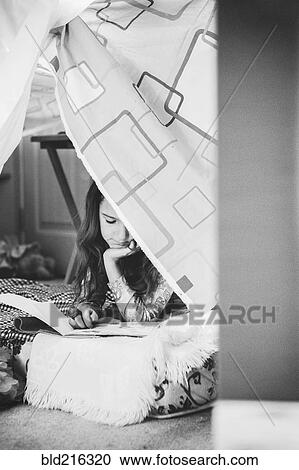 Stock Image - Caucasian girl reading in pillow fort. Fotosearch