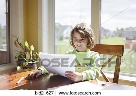Stock Image - Caucasian girl reading papers at table. Fotosearch