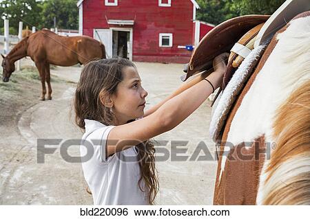 Stock Photograph - Caucasian girl saddling horse on ranch. Fotosearch