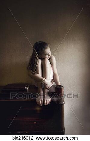 Stock Image - Caucasian girl sitting on dresser. Fotosearch