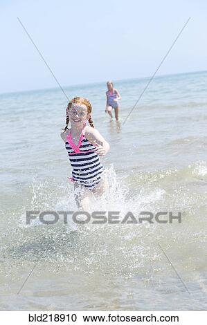 Stock Image - Caucasian girl splashing in waves on beach. Fotosearch
