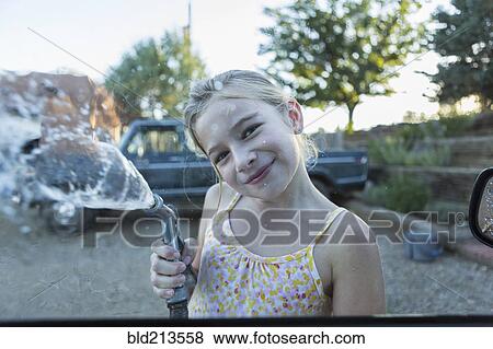 Stock Photo - Caucasian girl spraying water from hose outdoors. Fotosearch