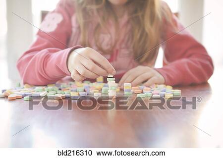 Stock Image - Caucasian girl stacking candy on table. Fotosearch