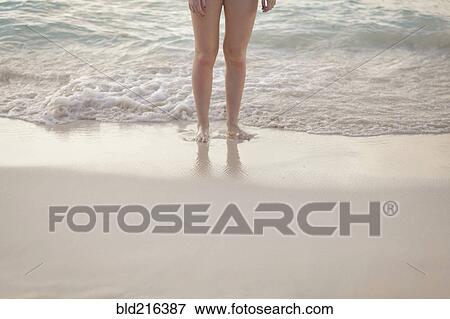 Stock Photo - Caucasian girl standing in waves on beach. Fotosearch