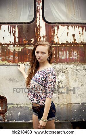 Stock Image - Caucasian girl standing near dilapidated bus. Fotosearch