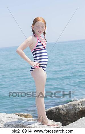 Picture - Caucasian girl standing on rocks on beach. Fotosearch