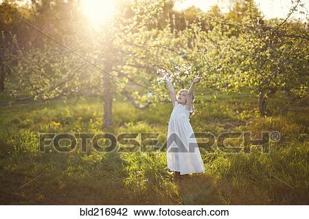 Stock Image - Caucasian girl tossing flower petals outdoors. Fotosearch