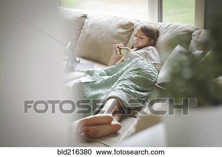 Stock Image - Caucasian girl using cell phone on sofa. Fotosearch