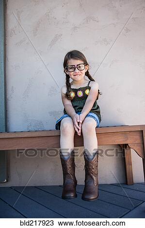 Stock Image - Caucasian girl wearing eyeglasses and cowboy boots on bench. Fotosearch