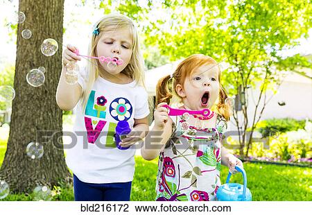 Stock Image - Caucasian girls blowing bubbles in background. Fotosearch