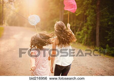 Stock Photograph - Caucasian girls carrying butterfly nets on dirt road. Fotosearch