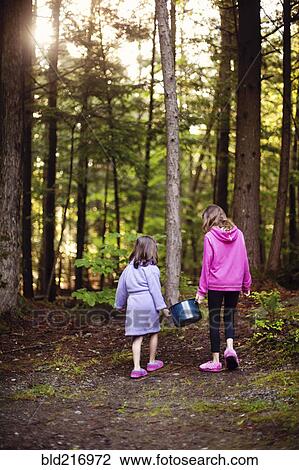 Stock Image - Caucasian girls carrying pot of water in forest. Fotosearch