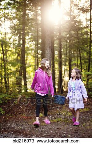 Stock Image - Caucasian girls carrying pot of water in forest. Fotosearch