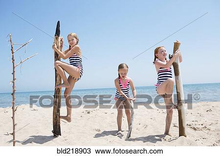 Stock Image - Caucasian girls climbing poles on beach. Fotosearch