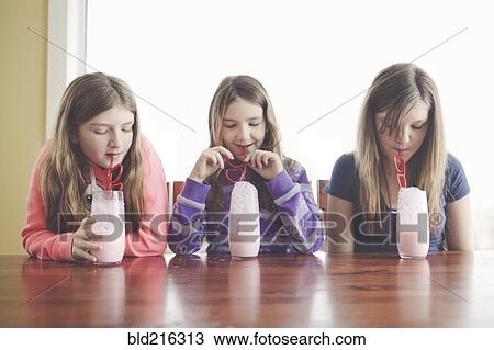 Stock Image - Caucasian girls drinking milk with curled straws at table. Fotosearch