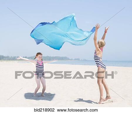 Stock Image - Caucasian girls playing with fabric on beach. Fotosearch
