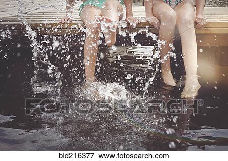 Stock Photo - Caucasian girls splashing in lake from wooden dock. Fotosearch