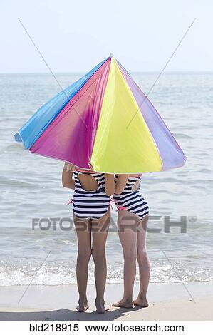Stock Photography - Caucasian girls under umbrella on beach. Fotosearch
