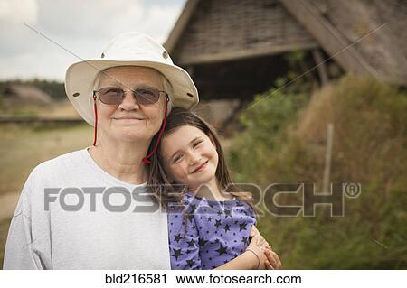 Stock Image - Caucasian grandmother hugging granddaughter in backyard. Fotosearch