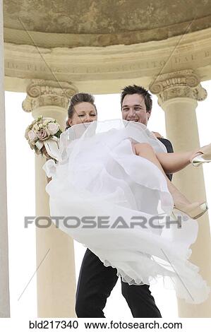 Stock Image - Caucasian groom carrying bride after wedding. Fotosearch