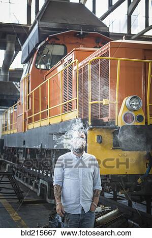 Stock Photo - Caucasian man blowing smoke in train yard. Fotosearch