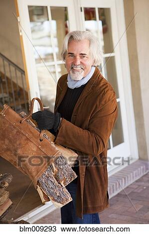 Stock Image - Caucasian man carrying firewood. Fotosearch