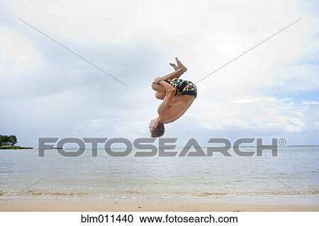 Stock Image - Caucasian man doing a flip on beach. Fotosearch