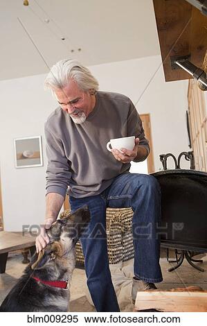 Stock Photography - Caucasian man drinking coffee and petting dog. Fotosearch